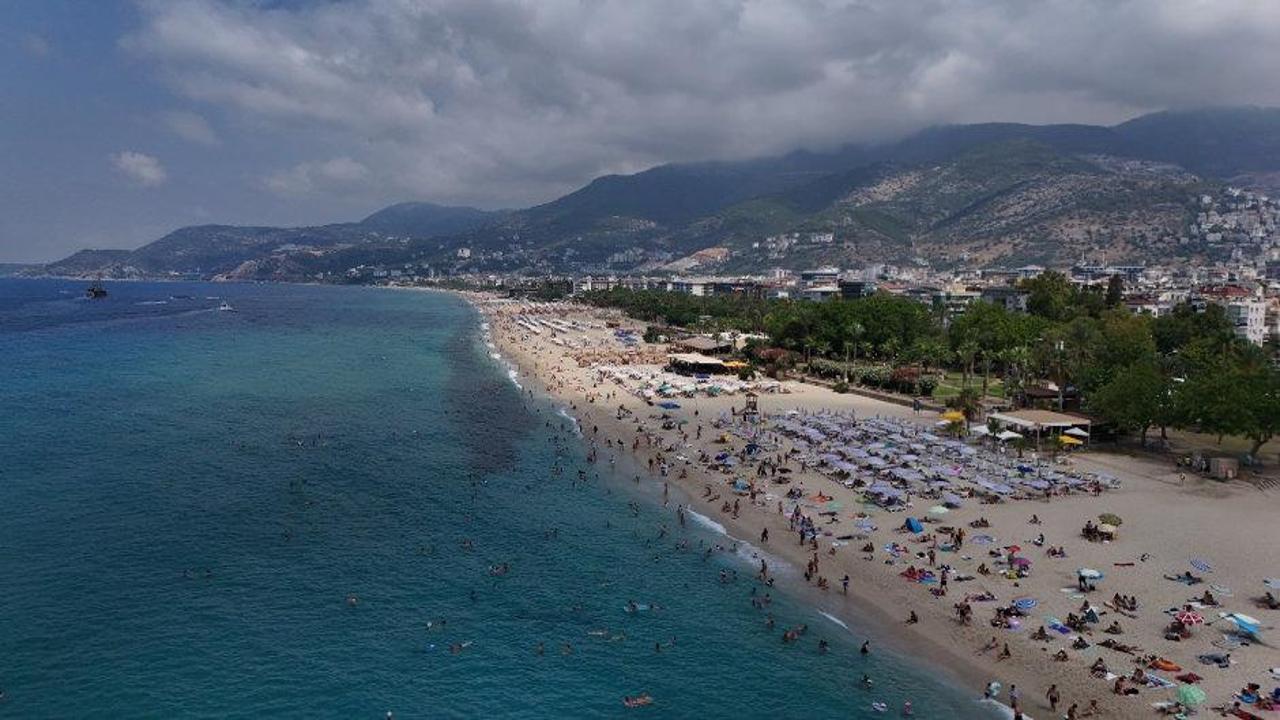 Alanya'da sıcak havada plajda güneşlenen ve denize giren turistler