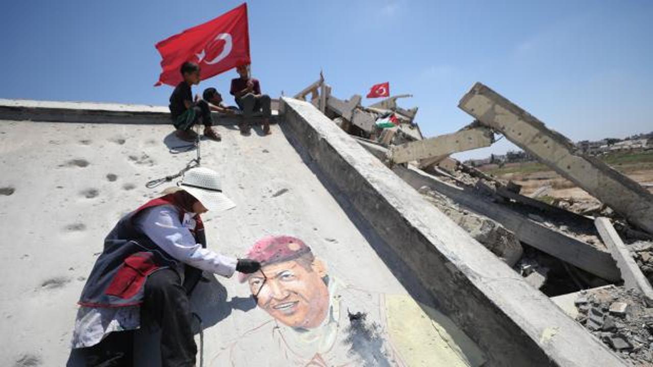 Gazze'deki Nusayrat Mülteci Kampı'nda yıkılan bir binanın duvarına çizilmiş Ömer Halisdemir resmi ve Türk-Filistin bayrakları taşıyan çocuklar.